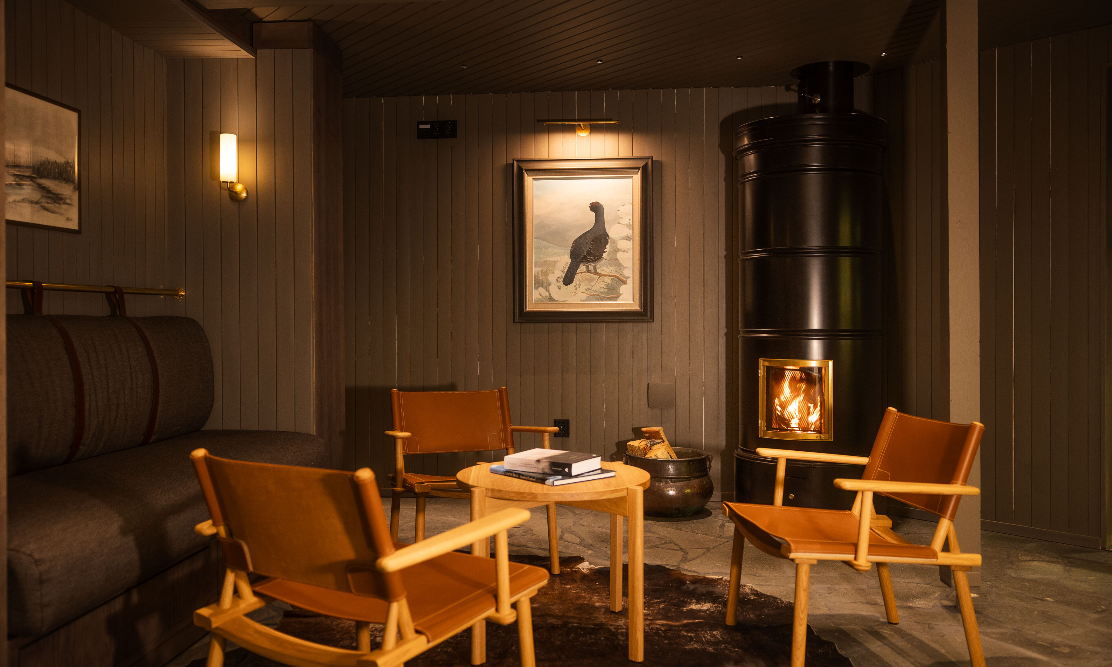 fireplace, chairs and table in dark interior of Aino's Guest Service lounge.