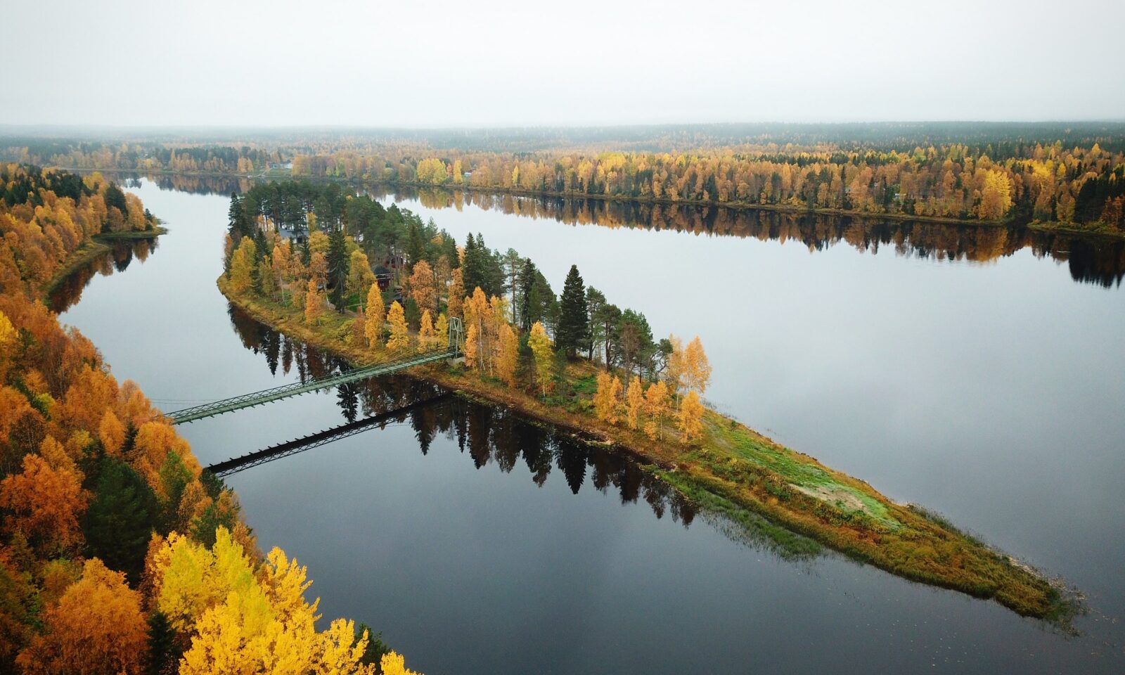Aerial view of Aino Private Island surrounded by calm water and golden autumn forest during ruska in Finnish Lapland.