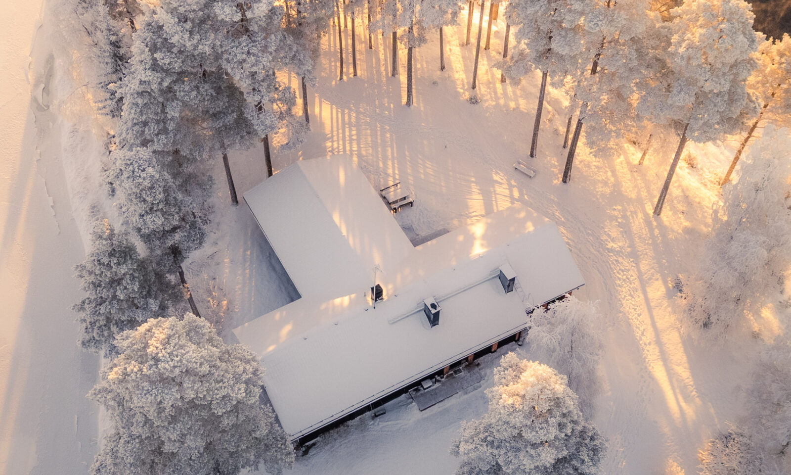 Aerial view of a snow-covered building at Aino Private Island surrounded by trees in soft winter sunlight.