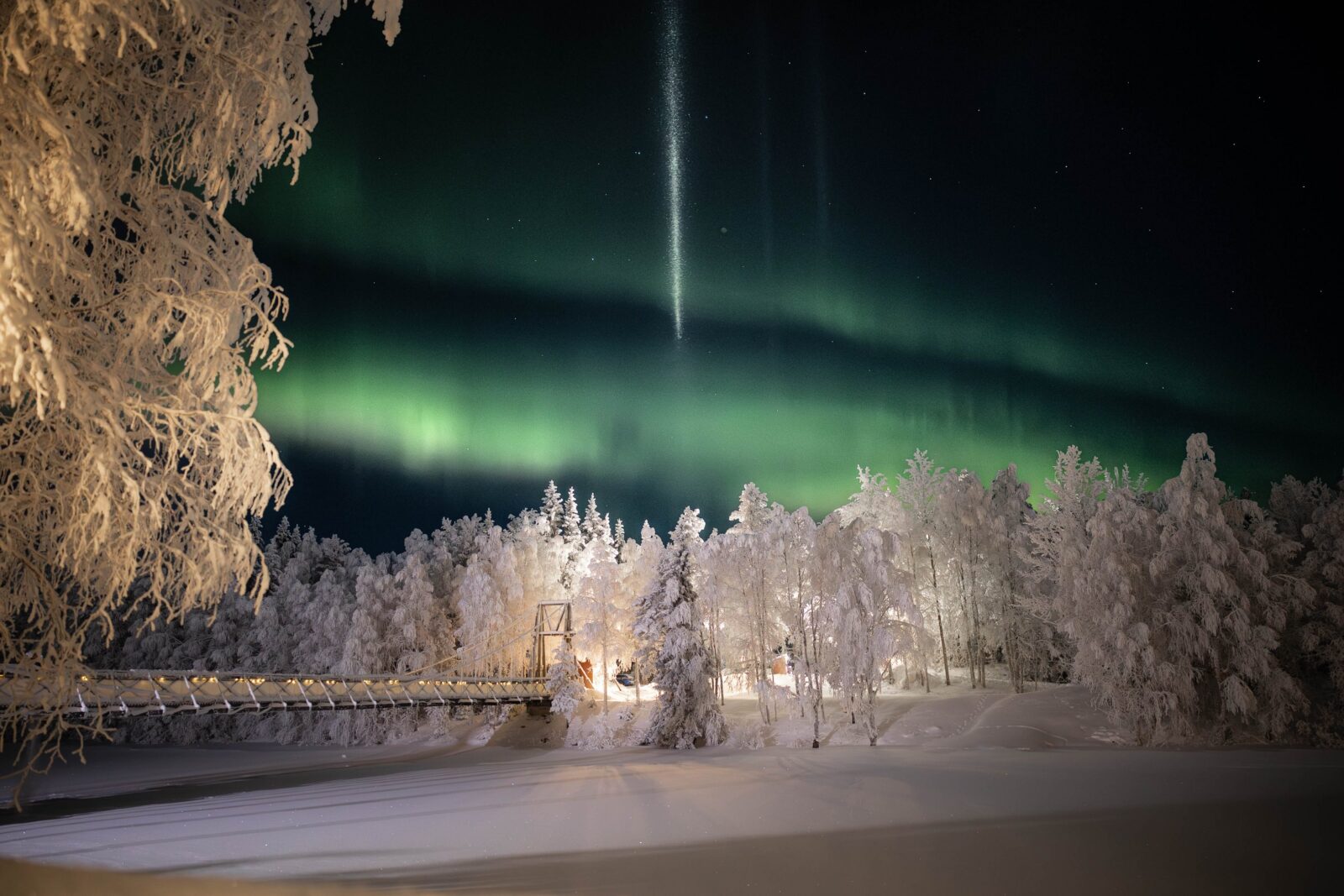 Northern Lights above the snow-covered bridge and forest at Aino Private Island in Rovaniemi, Finnish Lapland.