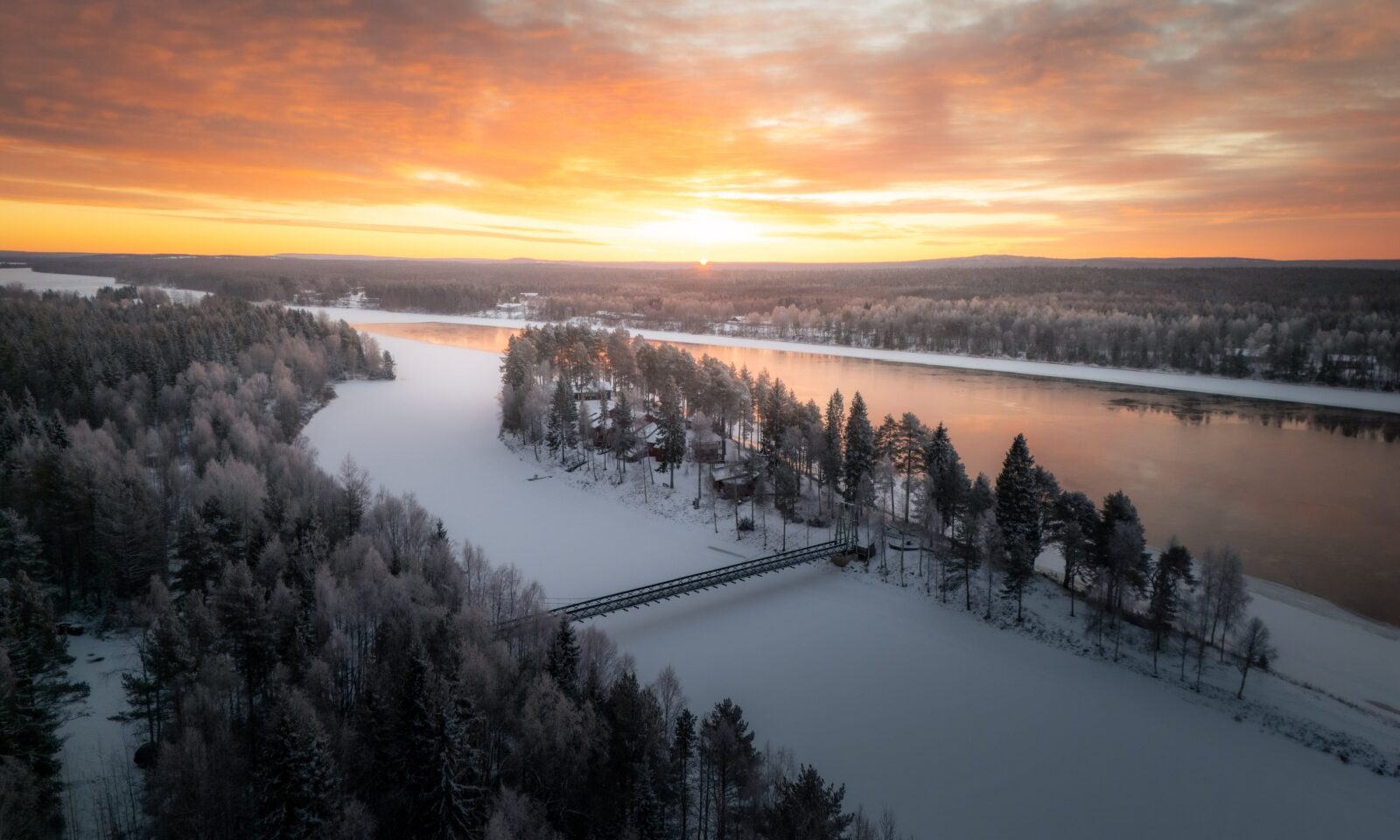 Aerial view of Aino Private Island at sunset, surrounded by snow-covered trees and calm winter water in Rovaniemi, Finnish Laplan